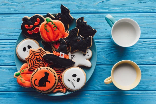 Vista superior de copos com leite e prato com deliciosos biscoitos caseiros de Halloween na mesa de madeira — Fotografia de Stock