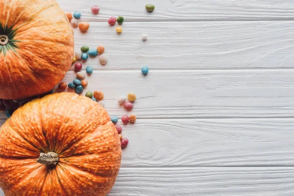 Vue de dessus des citrouilles et des bonbons colorés sur fond en bois — Photo de stock