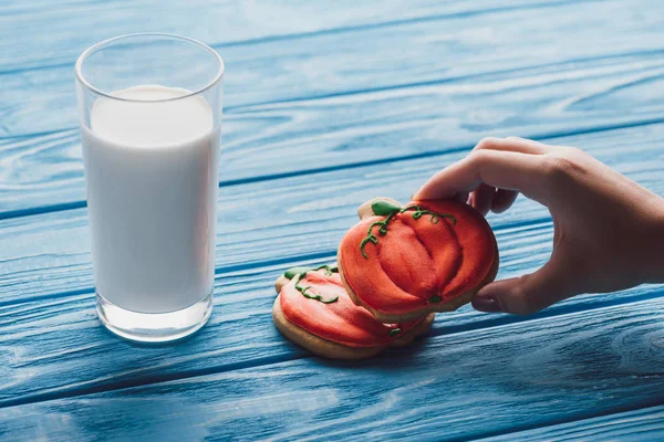 Abgeschnittenes Bild einer Frau, die köstliche halloowen Kürbisse in der Nähe eines Milchglases auf einem Holztisch nimmt — Stockfoto