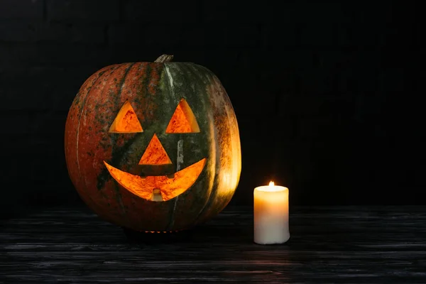 Gruseliger zu Halloween geschnitzter Kürbis mit Kerze auf Holztisch auf schwarzem Hintergrund — Stockfoto
