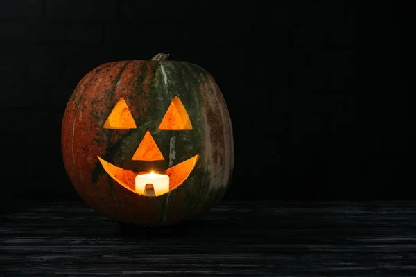 Jack o lantern pumpkin with candle inside on wooden table on black background — Stock Photo