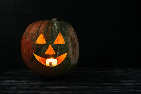 Jack o Laterne Kürbis mit Kerze drinnen auf Holztisch auf schwarzem Hintergrund — Stockfoto