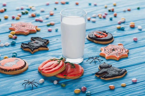 Vista de cerca de caramelos, galletas caseras de halloween y vaso de leche en la mesa de madera - foto de stock
