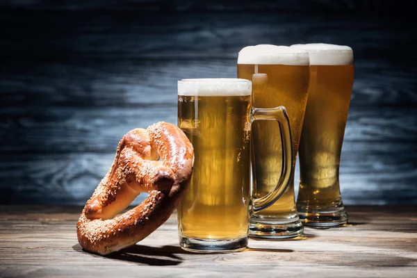 Три бокала пива с пеной и вкусный крендель на столе, oktoberfest концепции — стоковое фото