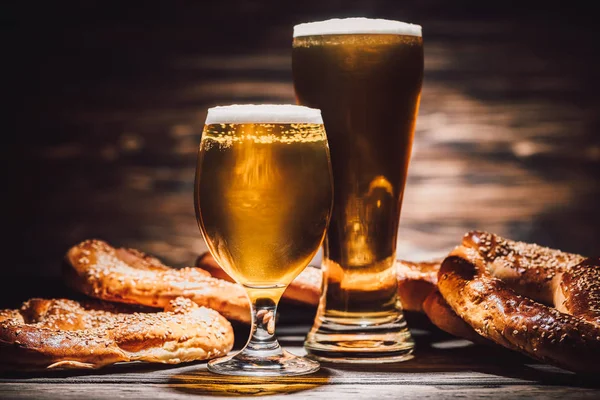 Dos vasos de cerveza y sabrosos pretzels sobre mesa de madera, concepto oktoberfest - foto de stock