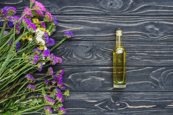 Draufsicht auf die Flasche mit natürlichem ätherischem Kräuteröl und violetten Blüten auf Holzoberfläche — Stockfoto