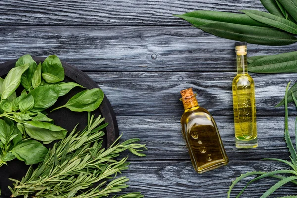 Top view of bottles with natural herbal essential oil and green leaves on wooden surface — Stock Photo