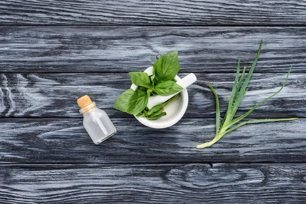 Elevated view of bottle of natural herbal essential oil, pestle with mortar and aloe vera on grey surface — Stock Photo