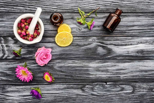 Vista superior de garrafas de óleos essenciais de ervas naturais, flores e pilão com argamassa na mesa de madeira — Fotografia de Stock