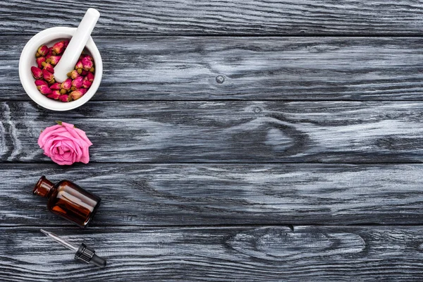 Erhöhte Ansicht der Flasche mit natürlichem ätherischem Kräuteröl, Tropfer und Rosen auf grauer Oberfläche — Stockfoto