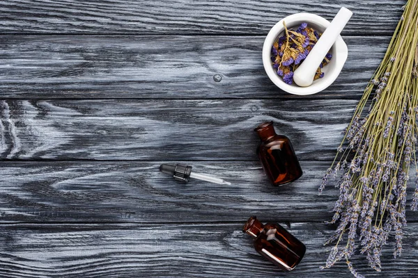 Vista superior de botellas de aceites esenciales de hierbas naturales, gotero y flores secas en la mesa de madera - foto de stock