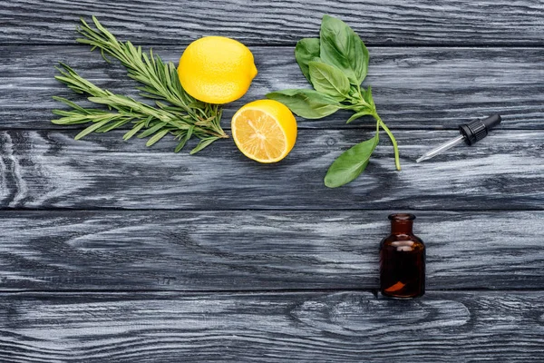 Vista elevata della bottiglia di olio essenziale naturale di erbe, contagocce e limoni sul tavolo di legno — Foto stock