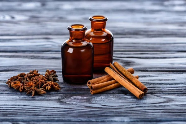 Garrafas de óleos essenciais de ervas naturais, cravo e paus de canela na mesa de madeira — Fotografia de Stock
