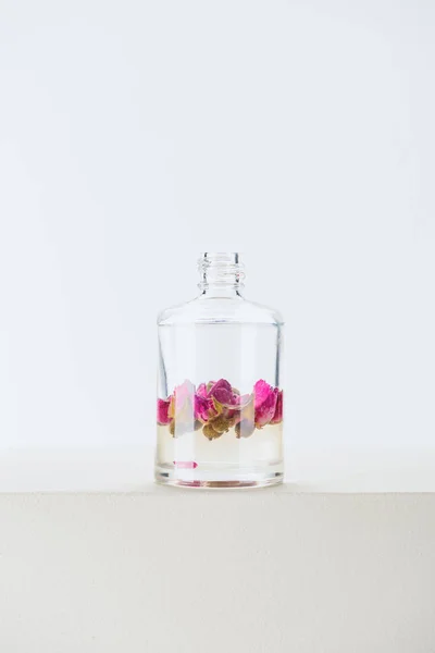 Бутылка натурального растительного эфирного масла с розовыми цветами на белой поверхности — стоковое фото