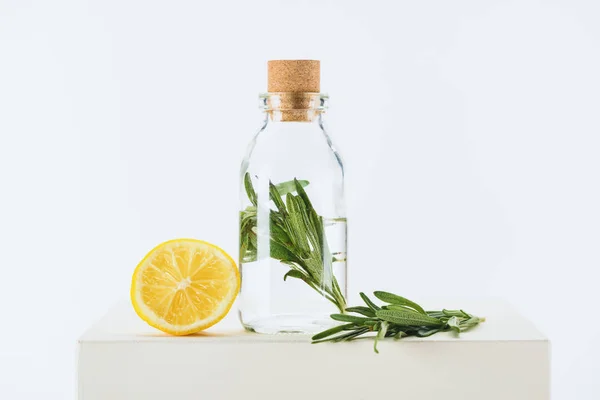 Bottle of natural herbal essential oil with green twig and lemon on white cube — Stock Photo