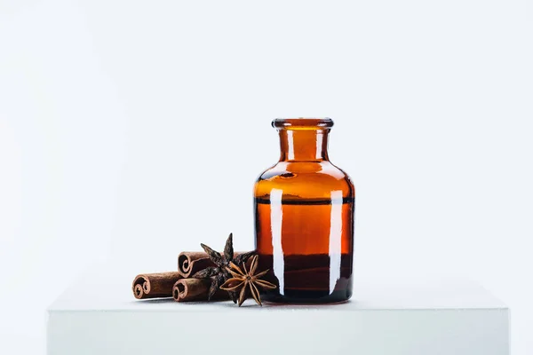 Bottle of natural herbal essential oil and carnation with cinnamon sticks on white cube — Stock Photo