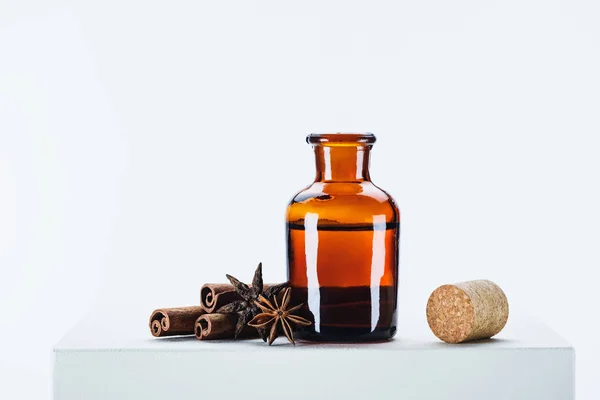 Bouteille d'huile essentielle naturelle à base de plantes, liège et œillet avec bâtonnets de cannelle sur cube blanc — Photo de stock