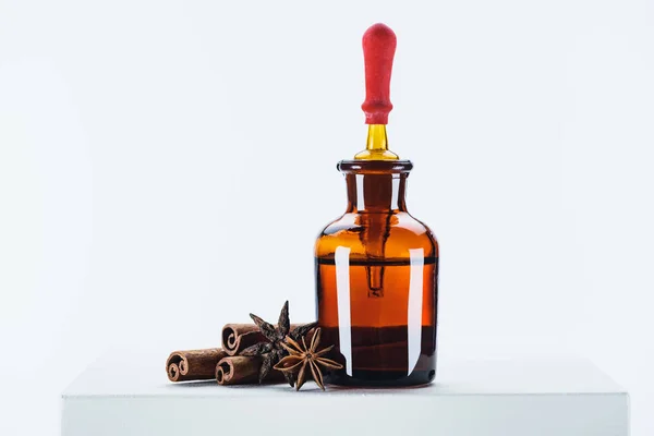 Бутылка натурального растительного эфирного масла, капельницы и гвоздики с корицей палочки на белом кубе — стоковое фото