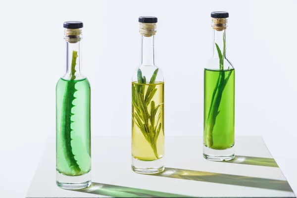 Bouteilles d'huiles essentielles vertes et jaunes avec des plantes sur la surface blanche — Photo de stock