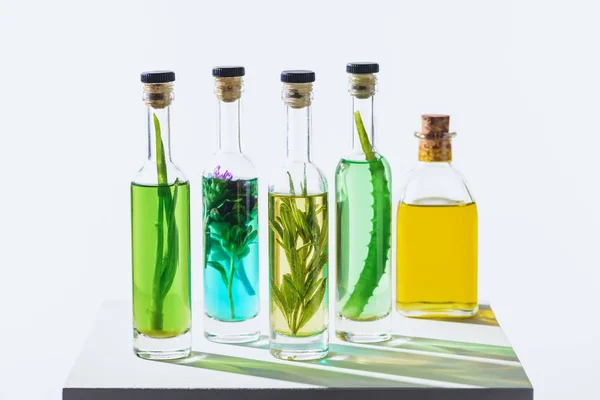 Frascos de aceites aromáticos esenciales verdes y amarillos con hierbas sobre cubo blanco - foto de stock