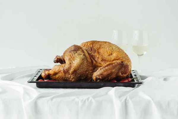 Close up view of cooked festive turkey on baking pan and glasses of wine on surface with tablecloth on grey background, thanksgiving holiday concept — Stock Photo