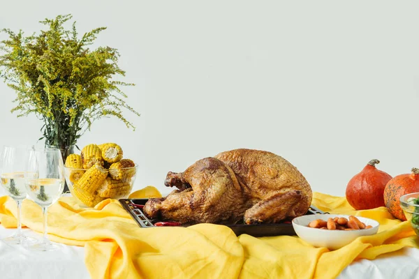 Vista de cerca del pavo festivo cocido en la bandeja para hornear, vasos de vino y calabazas en la superficie con mantel sobre fondo gris, concepto de vacaciones de acción de gracias - foto de stock