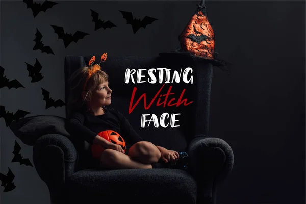 Очаровательный ребенок в костюме Хэллоуина отдыхает в кресле в темной комнате с надписью 