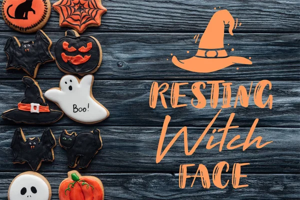 Erhöhter Blick auf arrangierte hausgemachte Plätzchen zu Halloween, die reihenweise auf schwarzem Holzgrund mit dem Schriftzug 