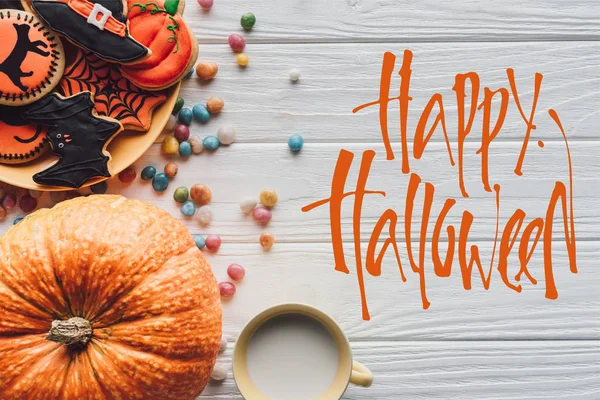 Elevated view of pumpkin, plate with halloween cookies, candies and cup with milk on wooden background  with 