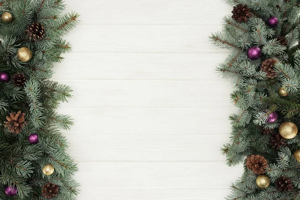 Beautiful evergreen fir twigs with shiny baubles and pine cones on white wooden background — Stock Photo