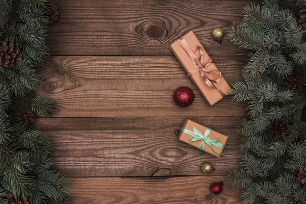Vista superior de presentes de Natal, bugigangas brilhantes e ramos coníferas com cones de pinho em fundo de madeira — Fotografia de Stock