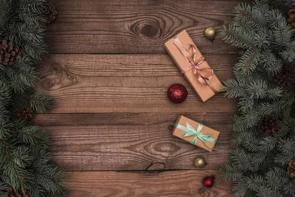 Top view of christmas presents, shiny baubles and coniferous branches with pine cones on wooden background — Stock Photo