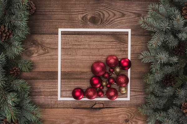 Vista superior de moldura branca, bolas vermelhas e douradas brilhantes e ramos coníferas com cones de pinho, fundo de natal — Fotografia de Stock
