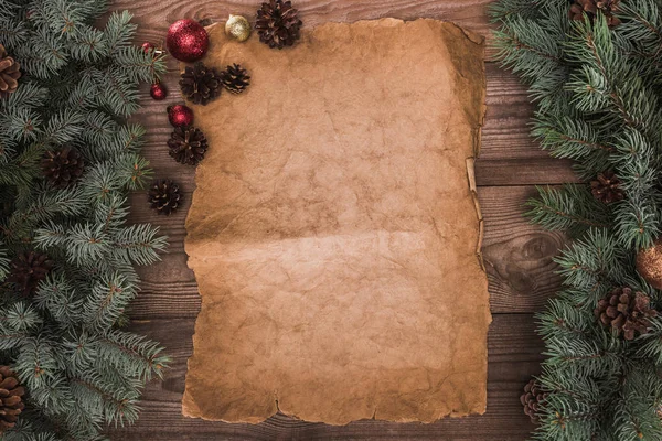 Blank parchment with fir twigs, shiny baubles and pine cones on wooden background — Stock Photo