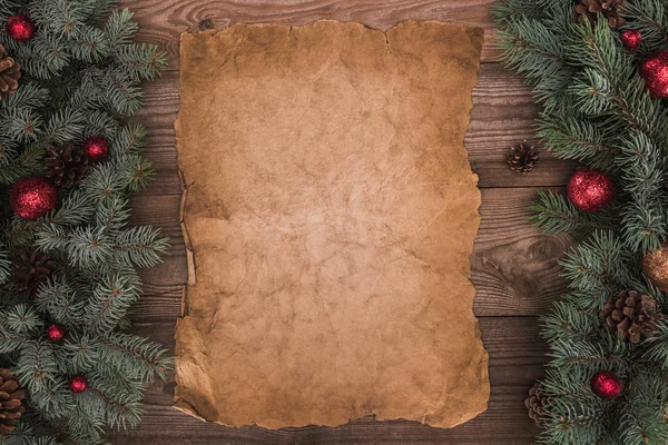 Close-up view of blank parchment with fir twigs, shiny baubles and pine cones on wooden background — Stock Photo