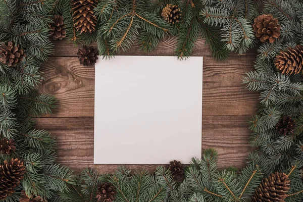 Vue du dessus de la carte vierge et des branches de conifères avec des cônes de pin sur fond en bois — Photo de stock