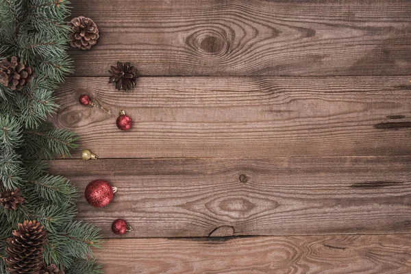 Vue de dessus des boules brillantes, des brindilles de conifères et des cônes de pin sur fond en bois — Photo de stock