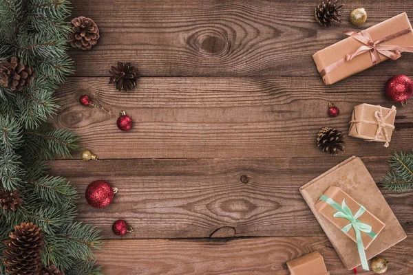 Top view of coniferous branches with pine cones, baubles and christmas presents on wooden background — Stock Photo