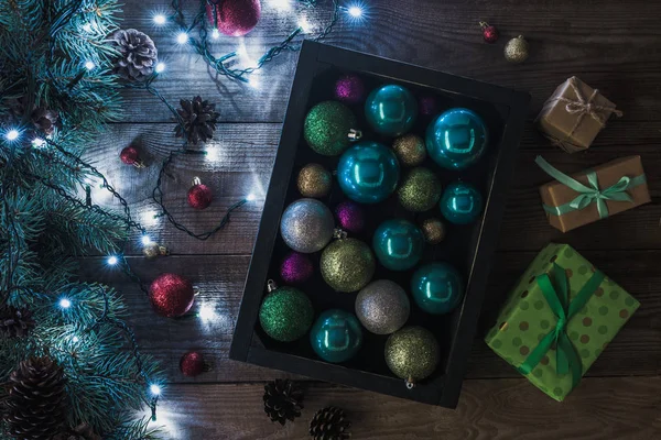 Blick von oben auf Weihnachtsgeschenke, glänzende Kugeln und Tannenzweige mit beleuchtetem Kranz auf Holzgrund — Stockfoto