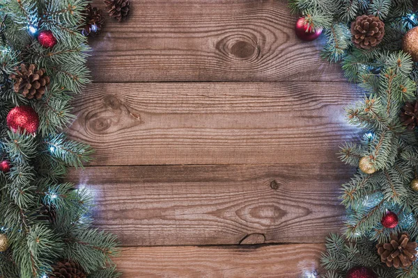 Hermosas ramas de árbol de Navidad con adornos, conos de pino y guirnalda iluminada sobre fondo de madera — Stock Photo