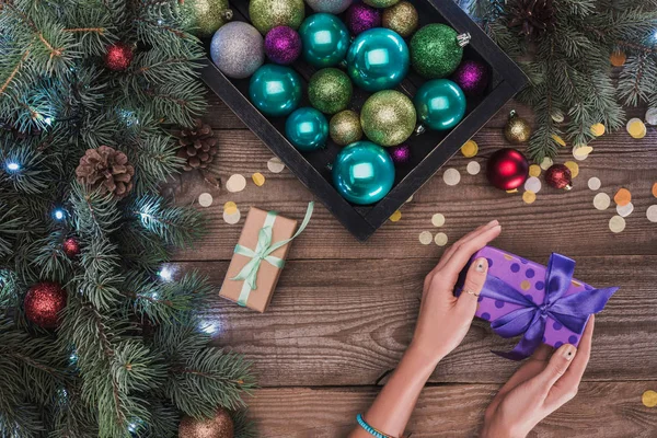 Cropped shot of christmas present in hands, shiny baubles and beautiful fir twigs with pine cones — Stock Photo