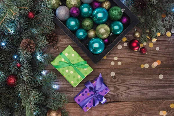 Vue de dessus de belles boules brillantes colorées, boîtes-cadeaux et brindilles de sapin sur fond en bois — Photo de stock