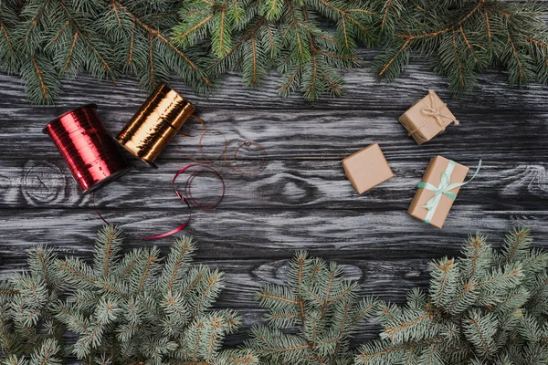 Vista superior de hermosas ramitas de abeto siempreverde, cajas de regalo y cintas brillantes sobre fondo de madera - foto de stock