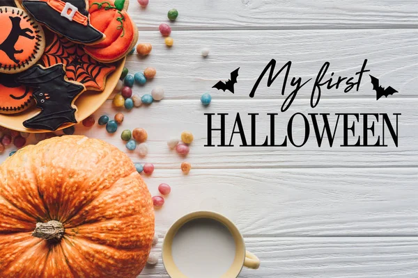 Vista elevada de la calabaza, plato con galletas de halloween, dulces y taza con leche sobre fondo de madera con murciélagos y letras de 
