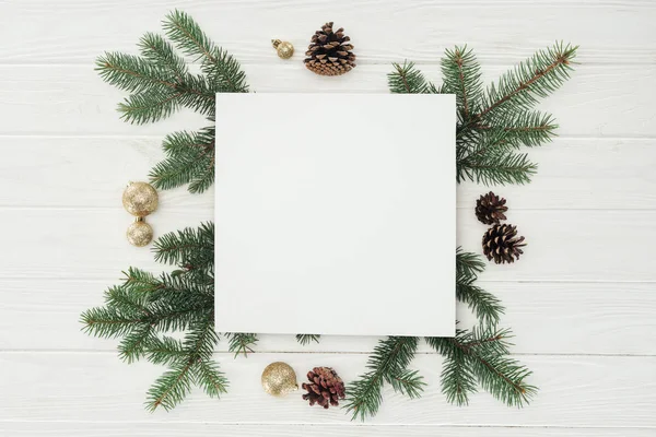 Draufsicht auf weiße Karte mit immergrünen Zweigen, Tannenzapfen und goldenen Weihnachtskugeln — Stockfoto