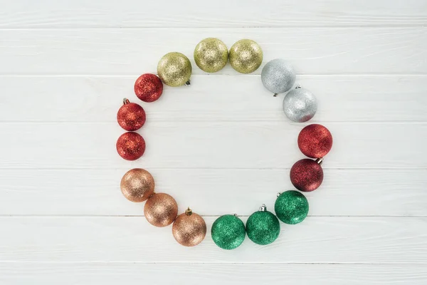 Top view of round frame made of beautiful shiny colorful christmas balls on white wooden surface — Stock Photo