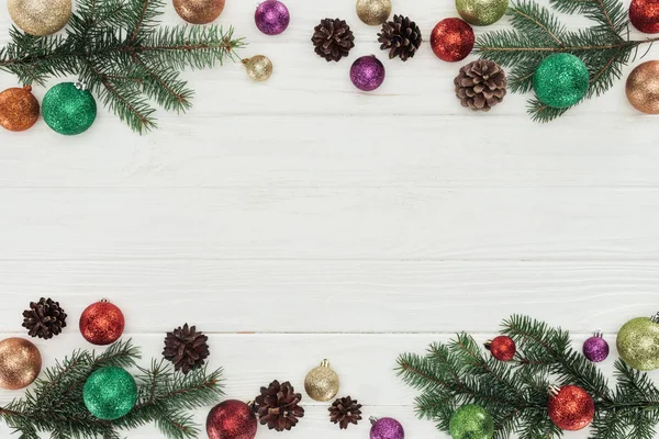 Vue de dessus des boules de Noël brillantes colorées, des brindilles de sapin et des cônes de pin sur fond de bois blanc — Photo de stock