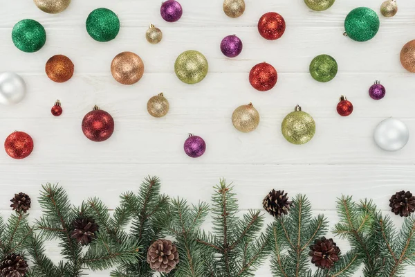 Belles boules de Noël colorées brillantes et brindilles de sapin avec cônes de pin sur fond blanc en bois — Photo de stock