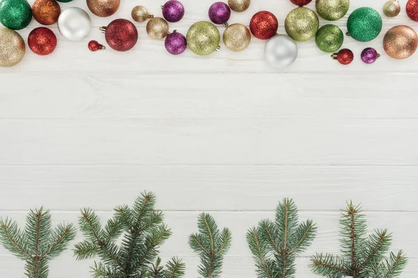 Top view of shiny colorful balls and green fir twigs on wooden surface, christmas background — Stock Photo