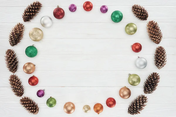 Top view of beautiful shiny colorful baubles and pine cones on wooden surface, christmas background — Stock Photo